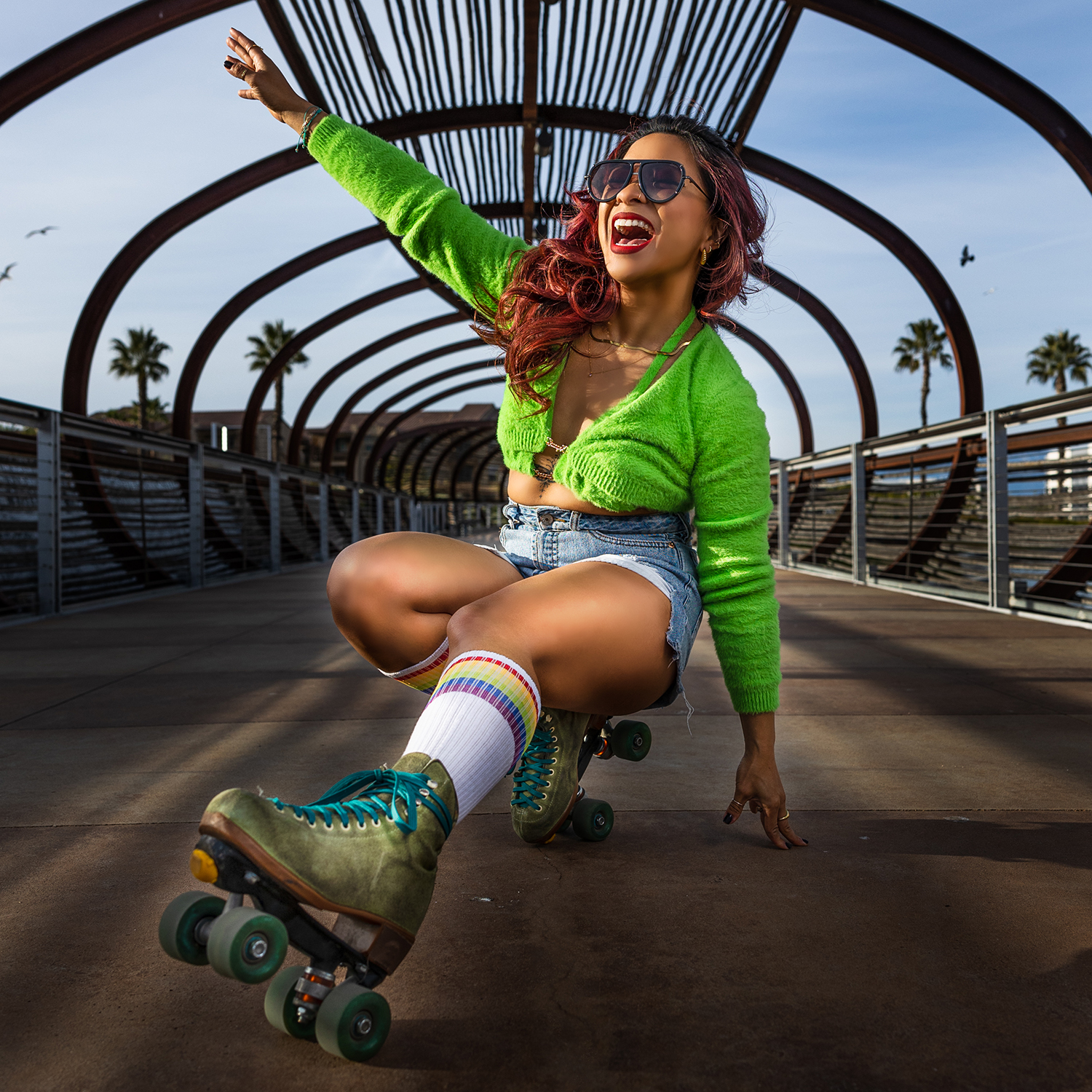 Phillapena woman wearing a green outfit with green rollerskates poses squatted down with left leg extended and right arm reaching up.